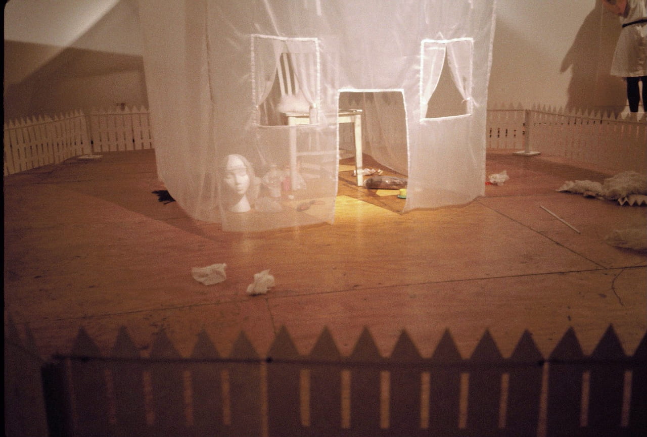 Installation view of sheer tent-house with chair, fence, and other props