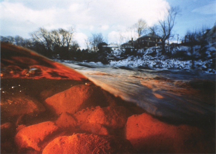 Half-underwater photo looking at rocks below and a house in snow above