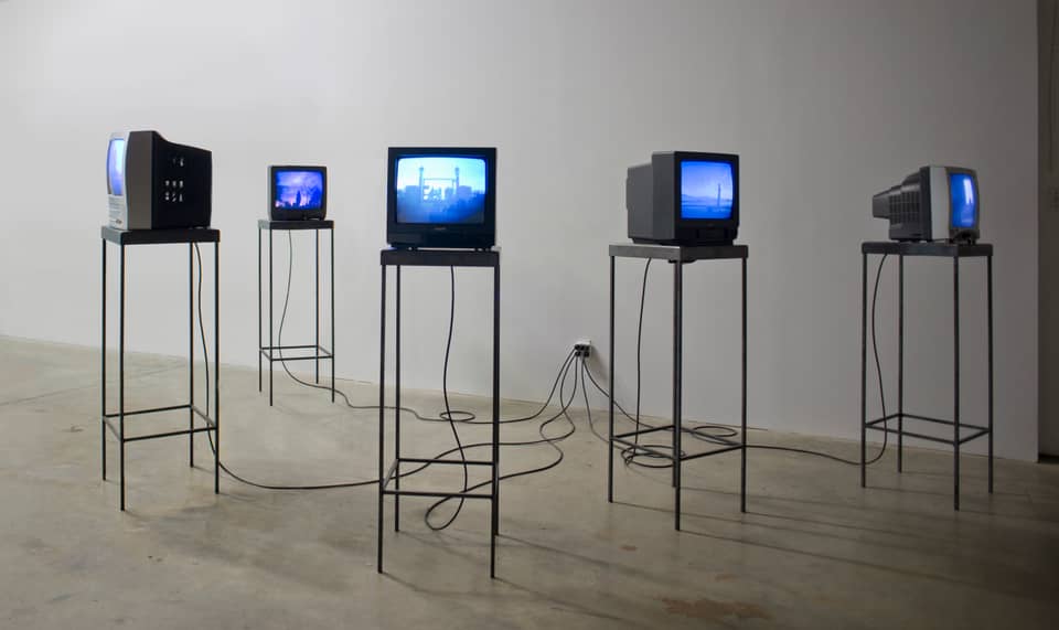 5 small TVs on tall metal stands, in a gallery