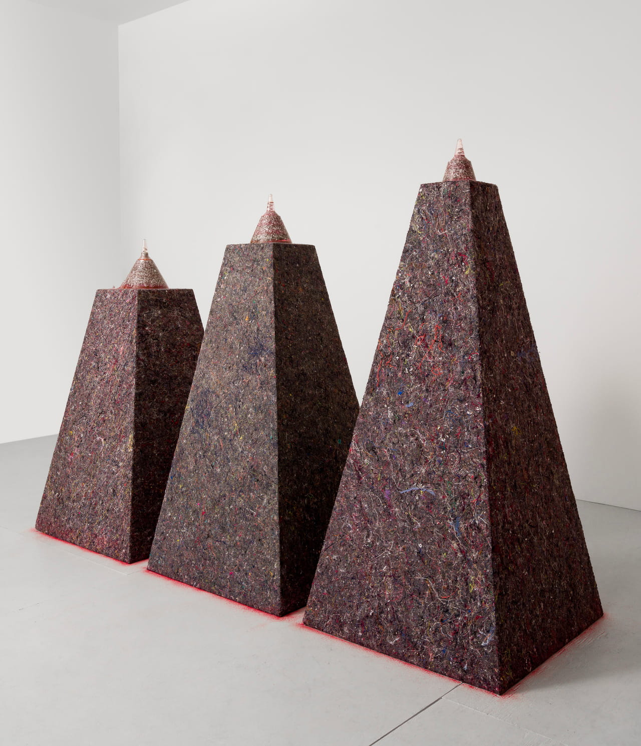 3 colorful, pyramidal plinths with resin cones sitting on them